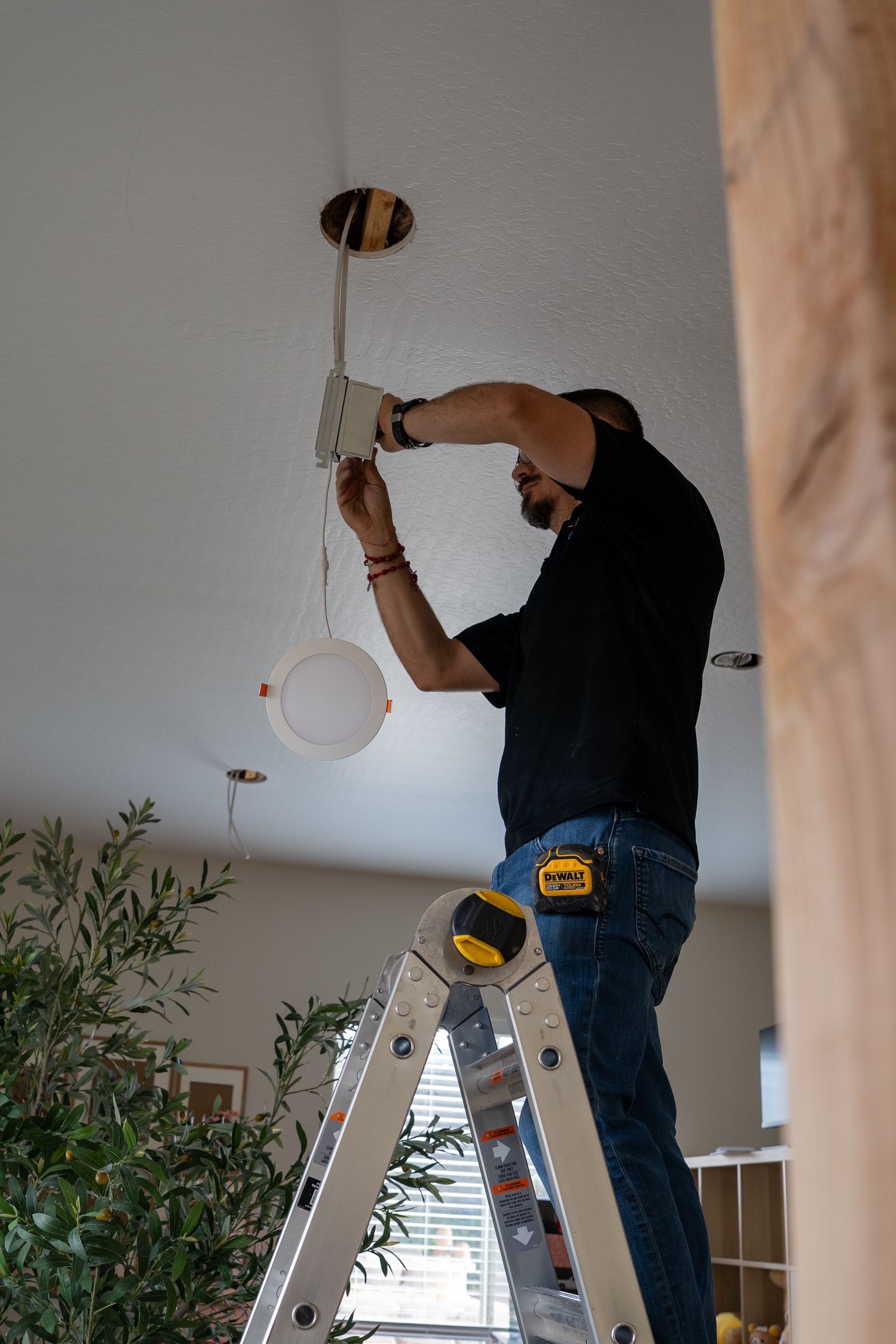 Person standing on a ladder installing a ceiling light fixture in a room