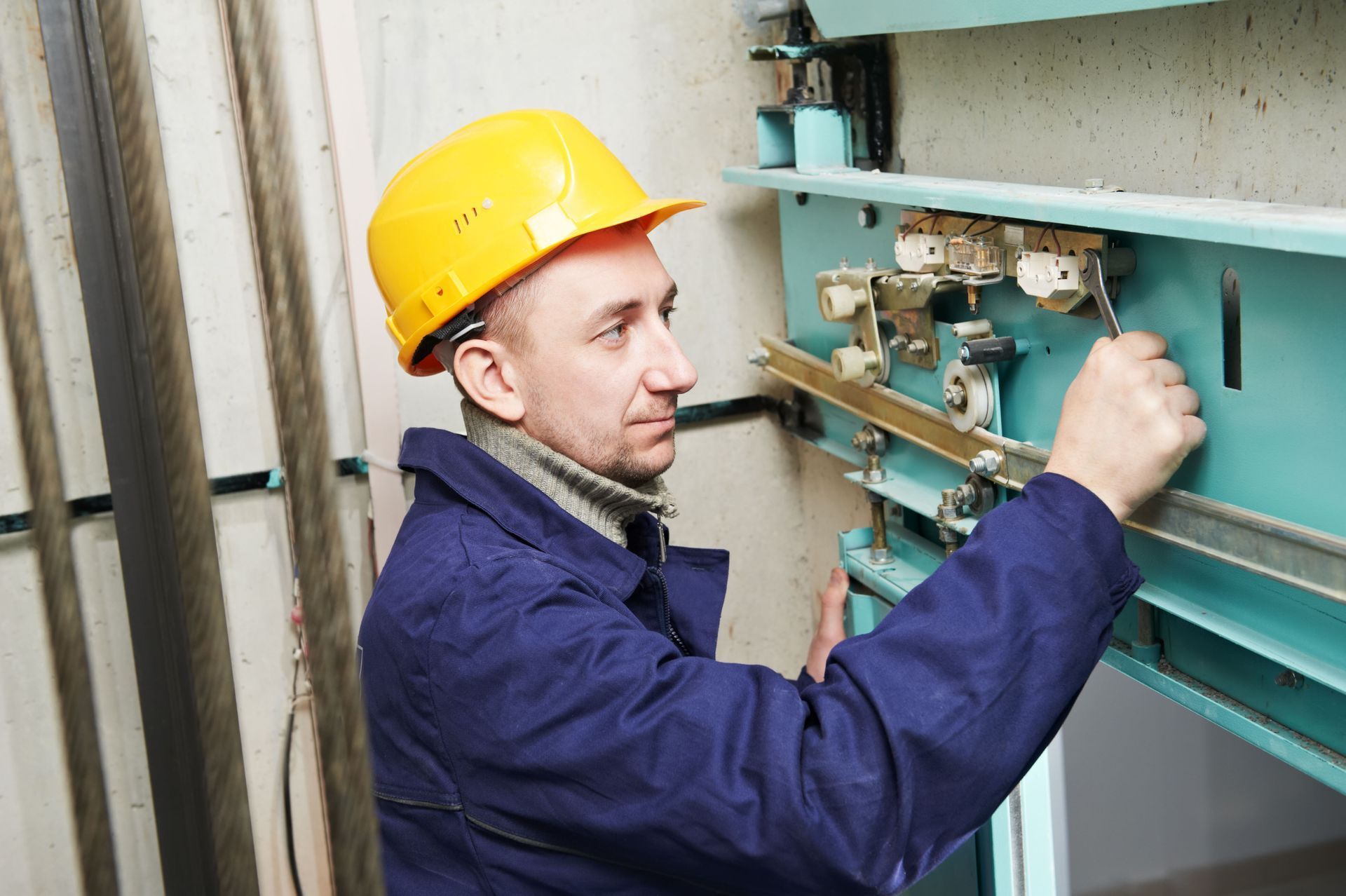 Technician in a yellow hard hat adjusting electrical panel wiring indoors