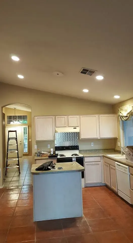 Bright kitchen with white cabinets, terracotta tile floor, island, and recessed ceiling lights.
