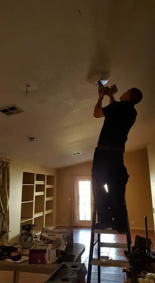 Person on a ladder fixing a ceiling light in a mostly empty room