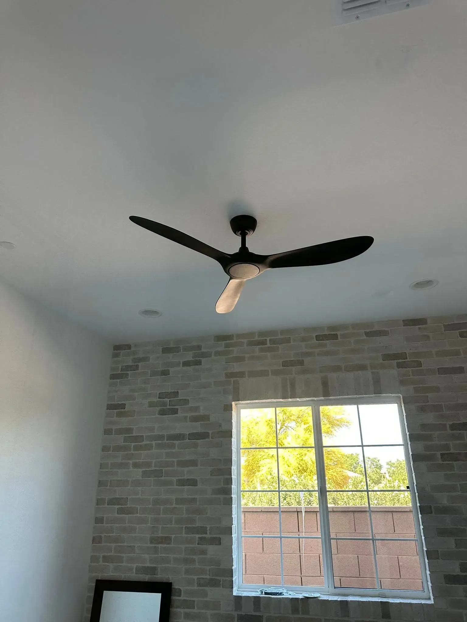 Interior room with black ceiling fan, brick accent wall, and a window with daylight