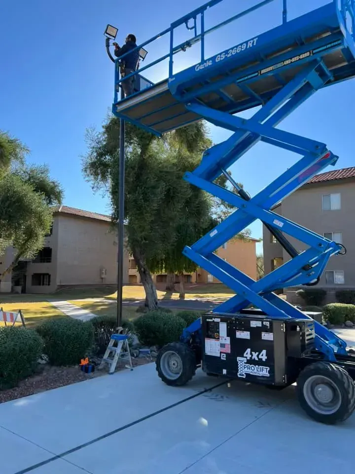 Worker on blue scissor lift trimming a tall palm tree in a suburban driveway