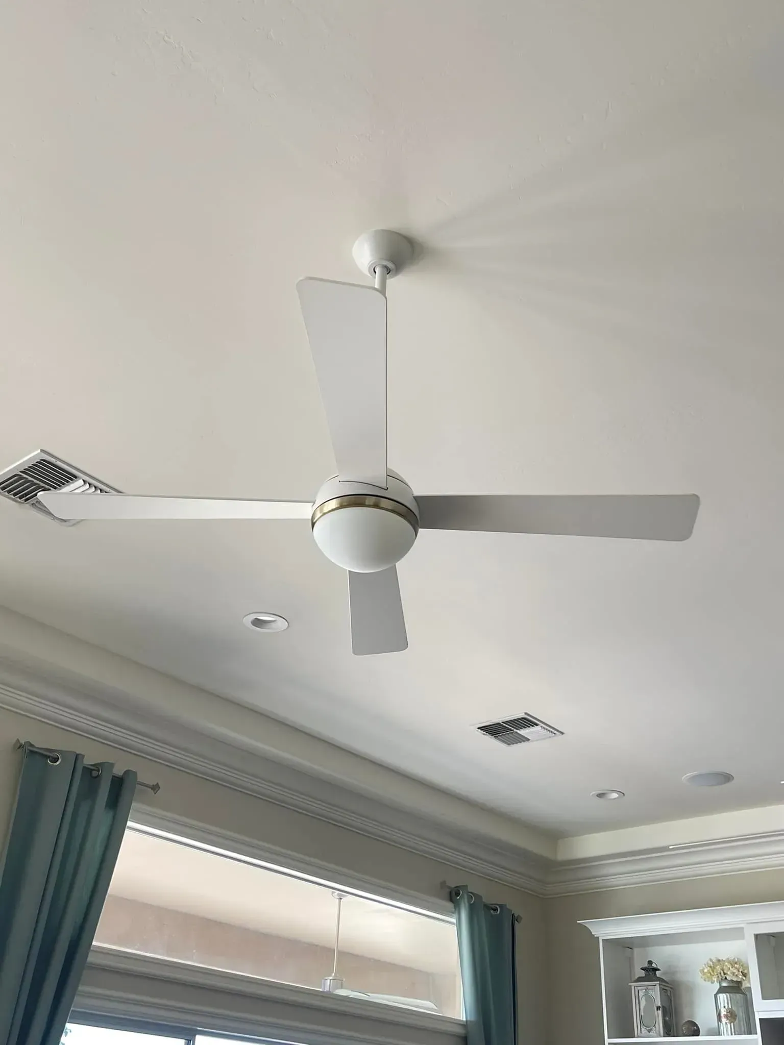 White ceiling fan centered above windows with teal curtains in a bright room