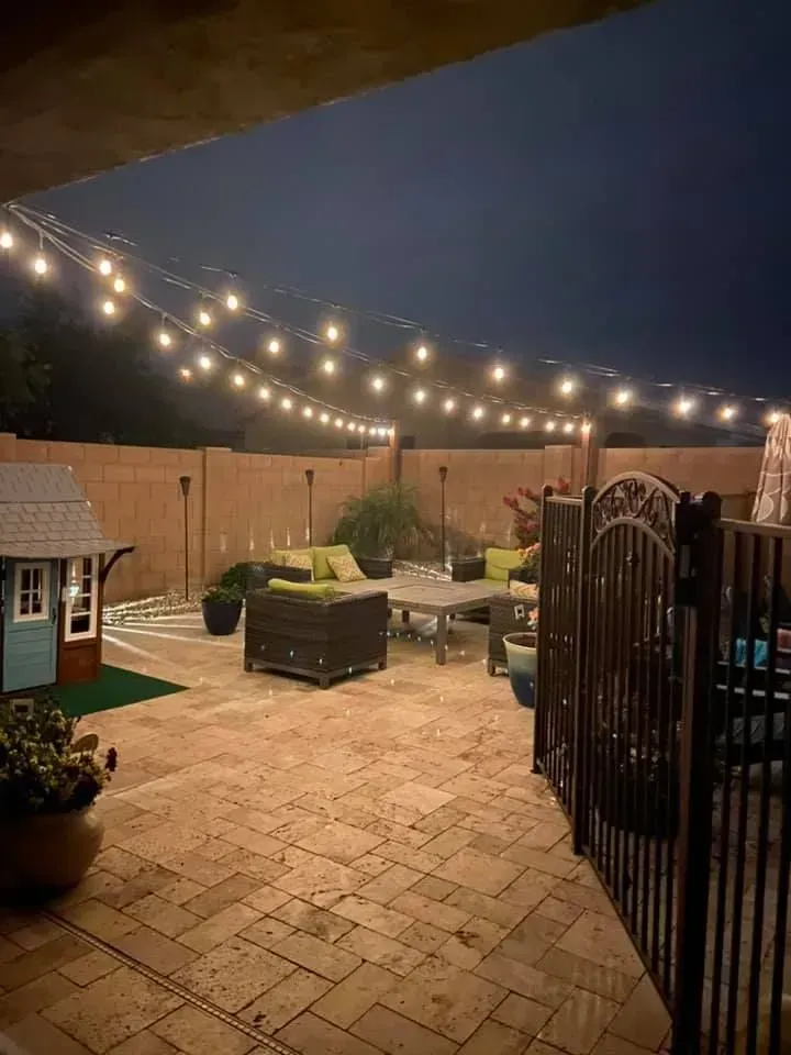 Backyard patio at night with string lights, brick paving, seating, and a small playhouse.