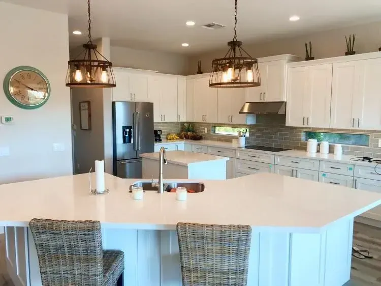 Bright modern kitchen with white cabinets, large island, pendant lights, and wicker stools