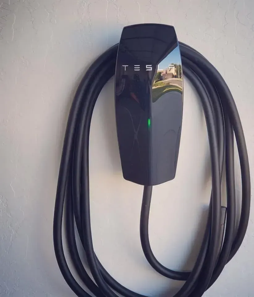 Tesla wall charger with black coiled cable mounted on a wall, showing a green status light