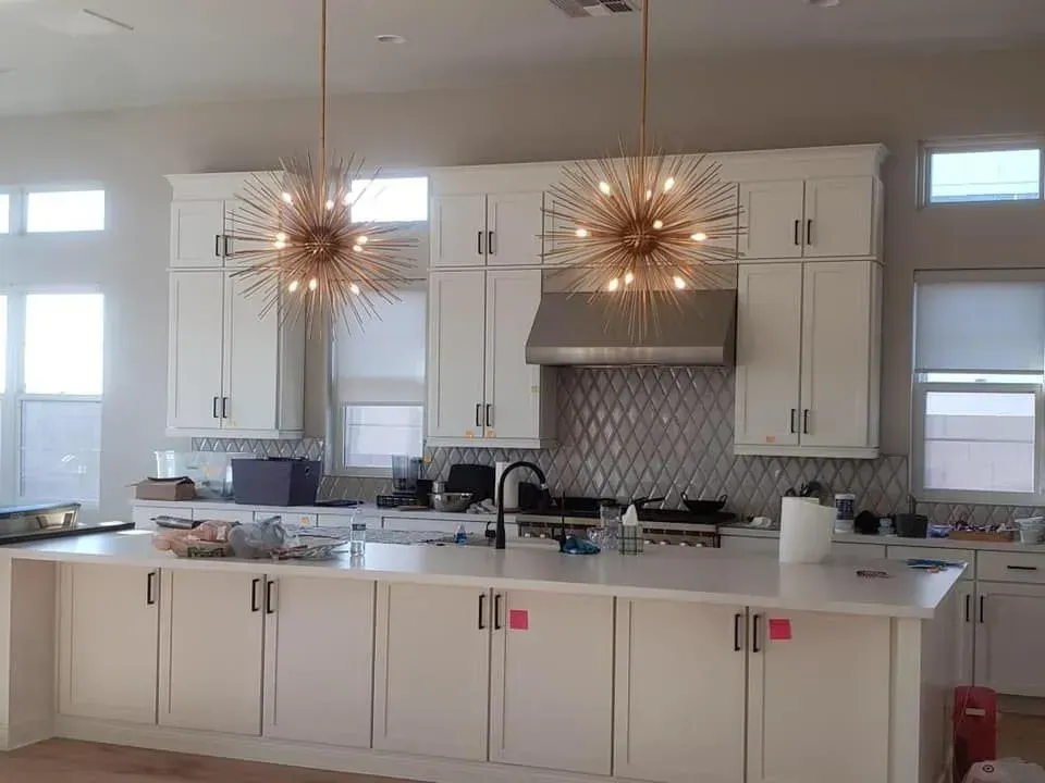 Modern white kitchen with island, pendant lights, stainless range hood, and windows on both sides