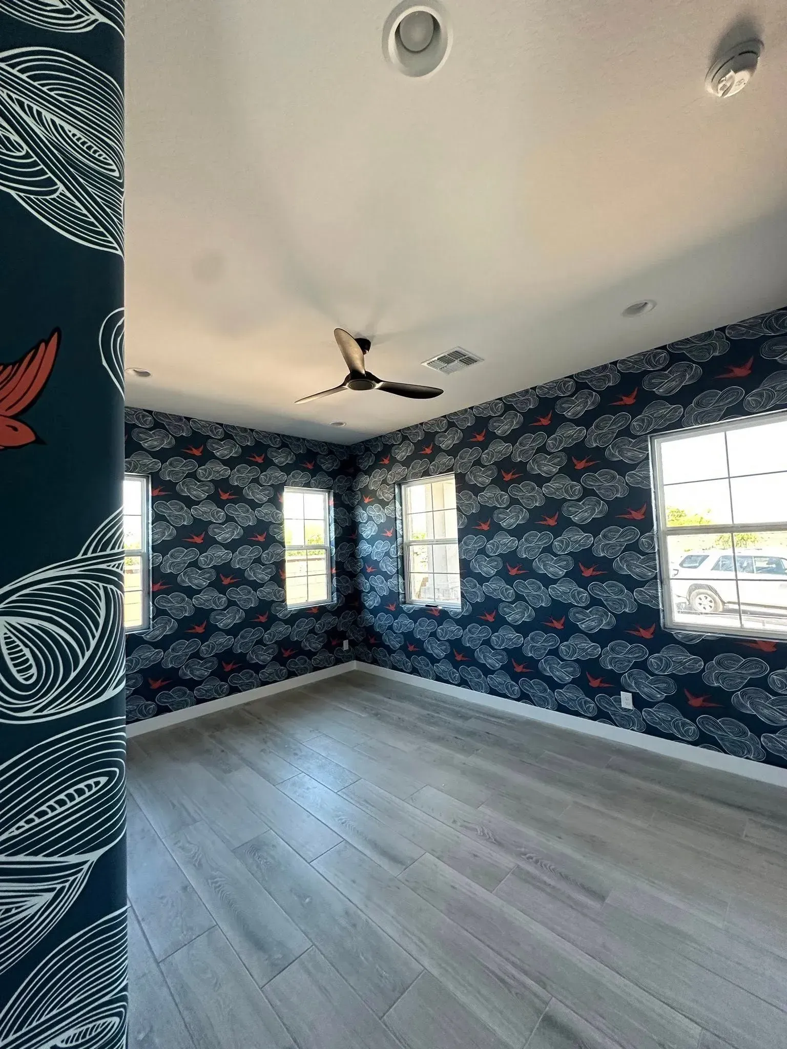 Empty room with dark floral wallpaper, light wood floors, and multiple windows.