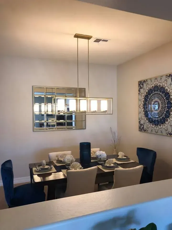 Modern dining room with set table, blue chairs, mirror, pendant light, and wall art