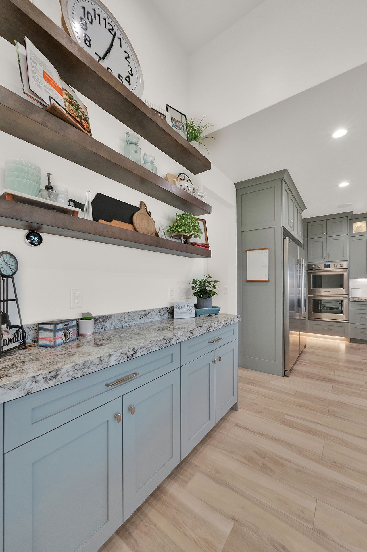 A kitchen with blue cabinets , granite counter tops , and a clock on the wall.