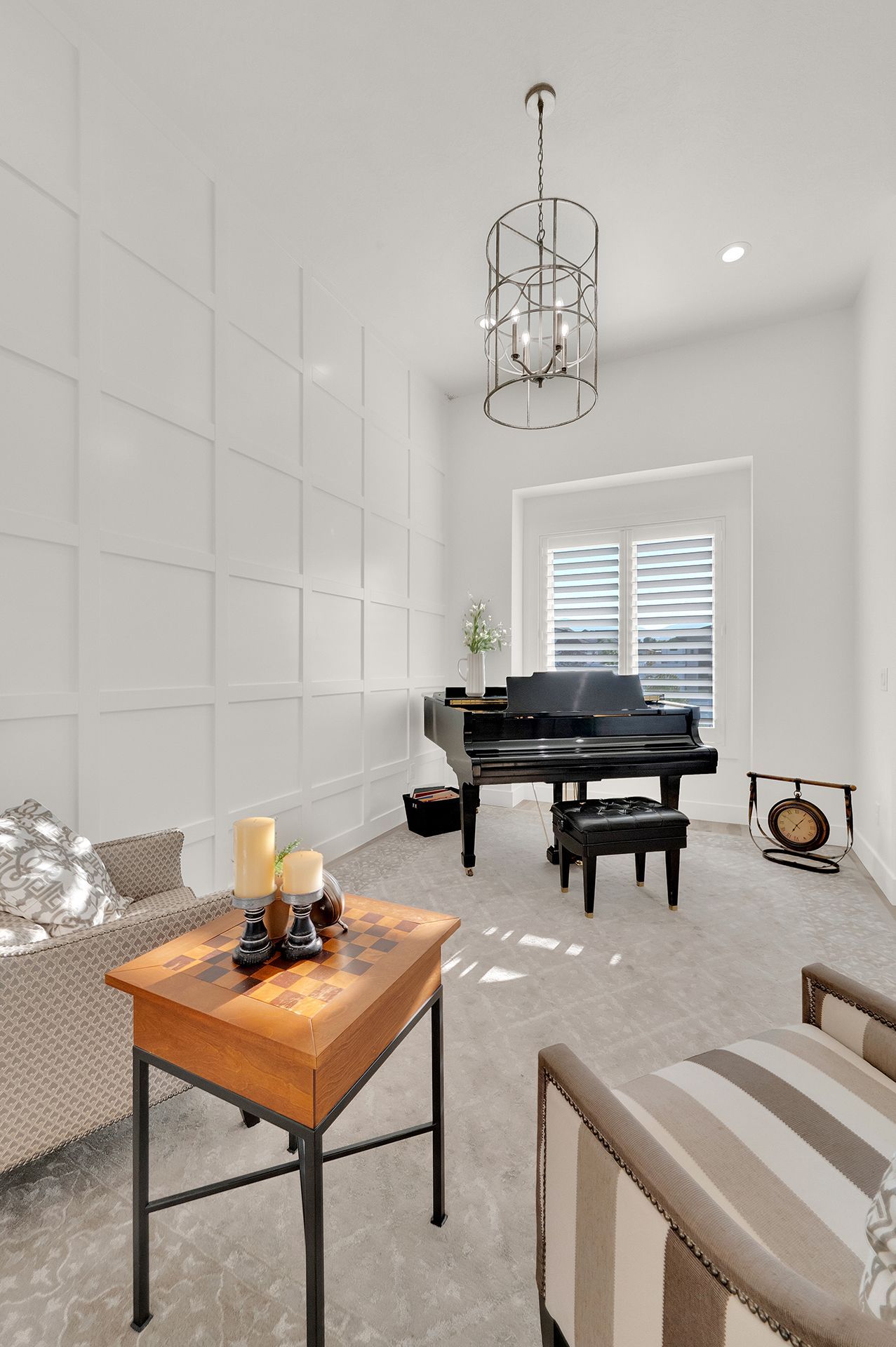 A living room with a piano , chair , table and chandelier.