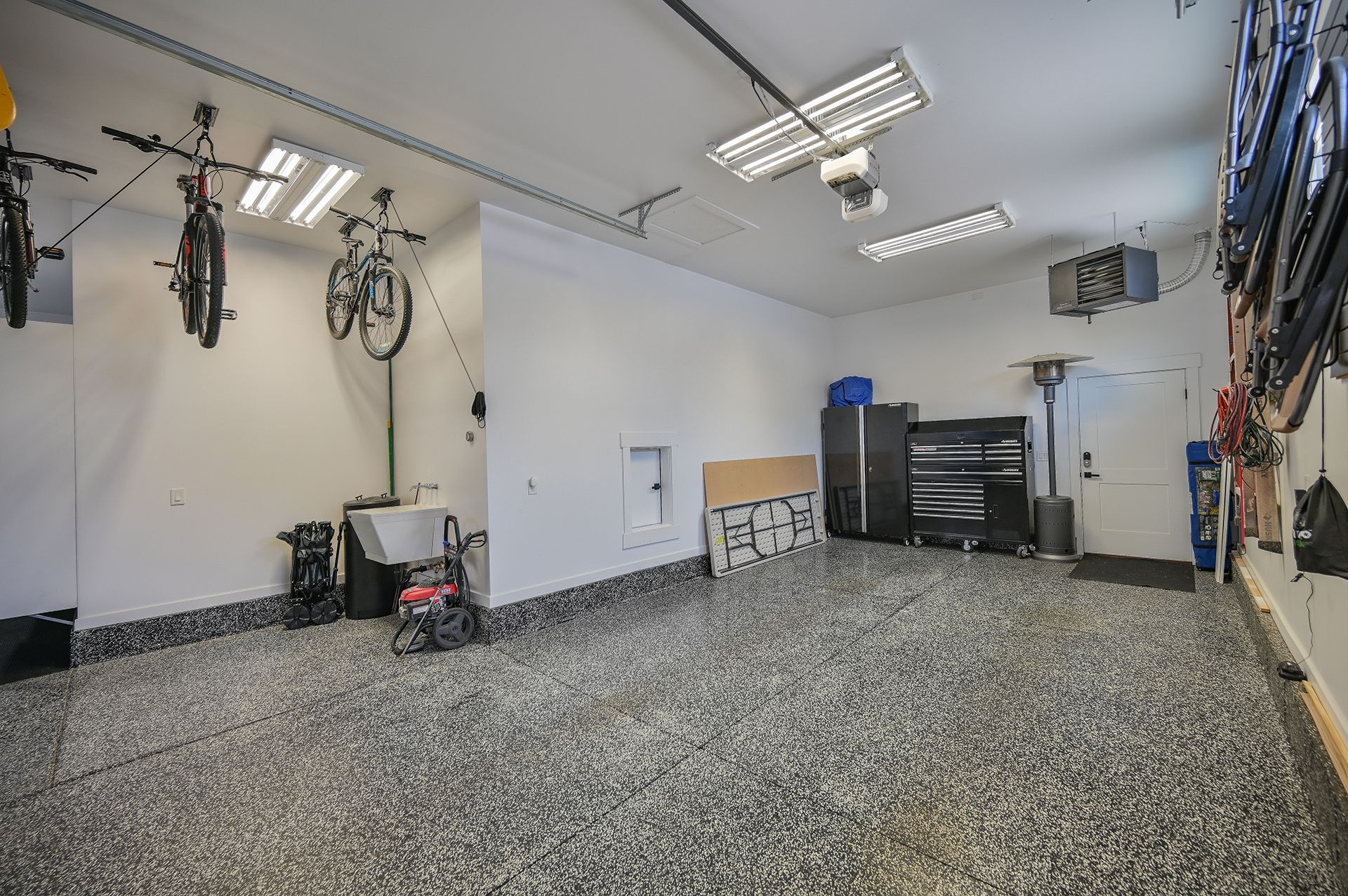 A garage with bikes hanging from the ceiling and a sink.