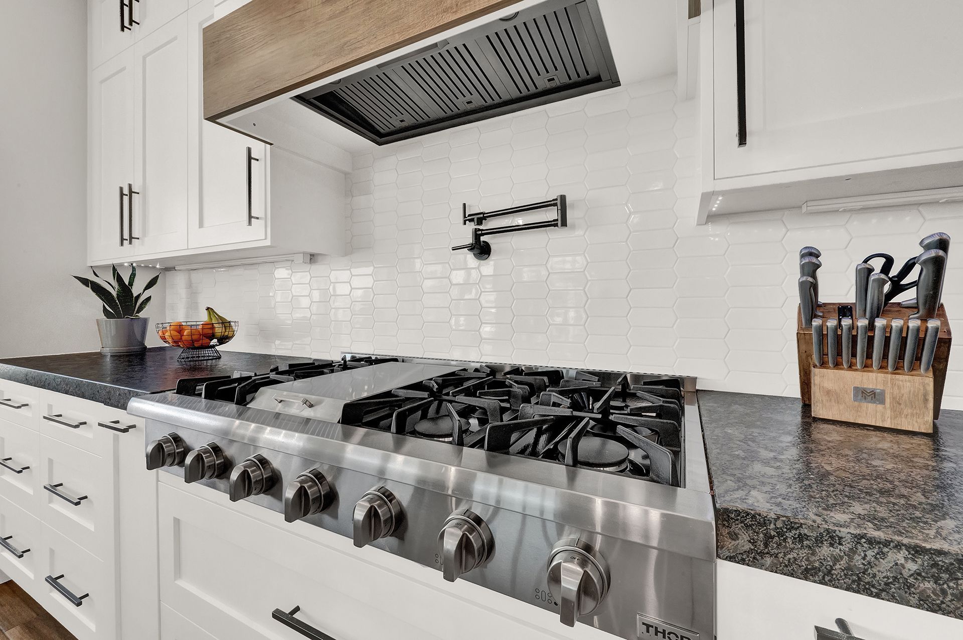 A kitchen with a stove top oven , granite counter tops , and white cabinets.