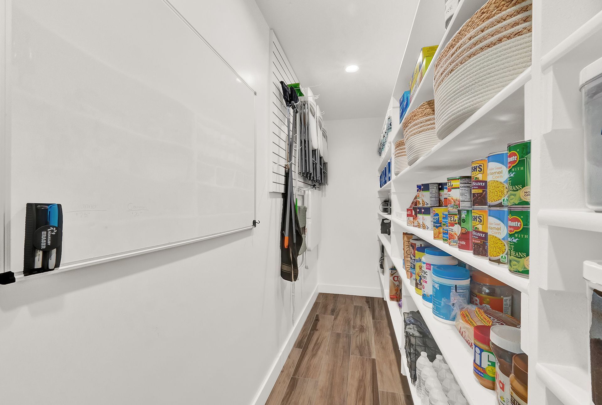 A walk in pantry with lots of shelves and a white board.