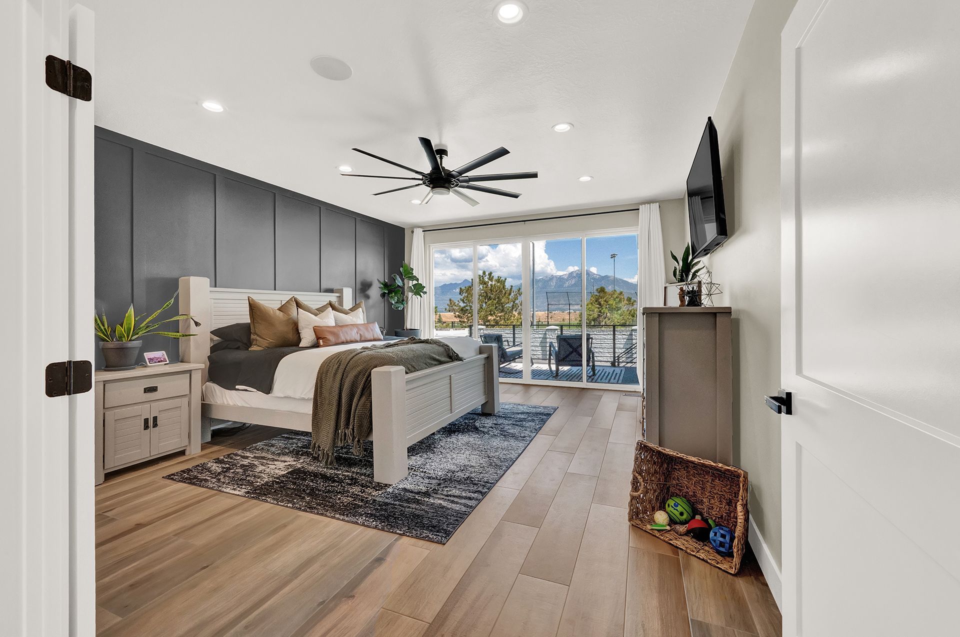 A bedroom with hardwood floors , a large bed , a ceiling fan and a flat screen tv.