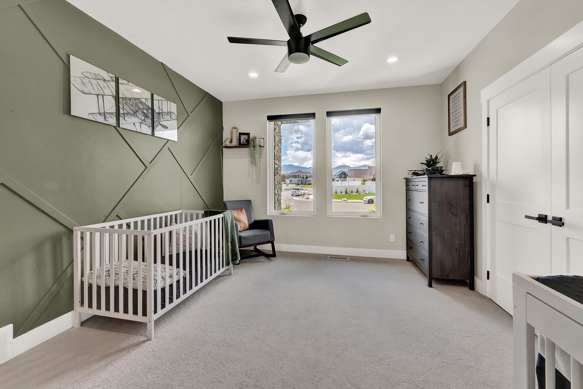 A bedroom with a crib , dresser , chair and ceiling fan.