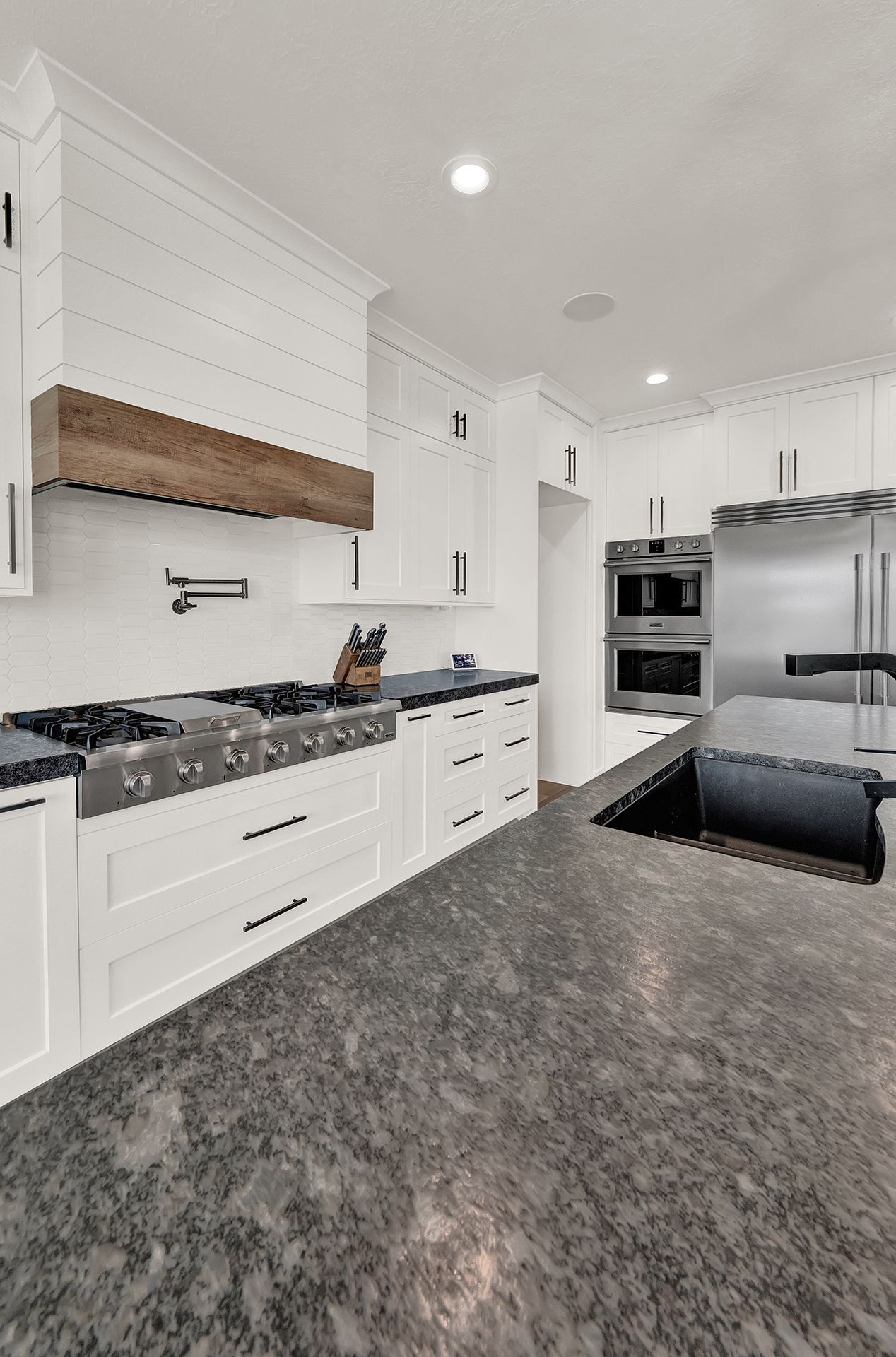 A kitchen with white cabinets , stainless steel appliances , granite counter tops and a sink.