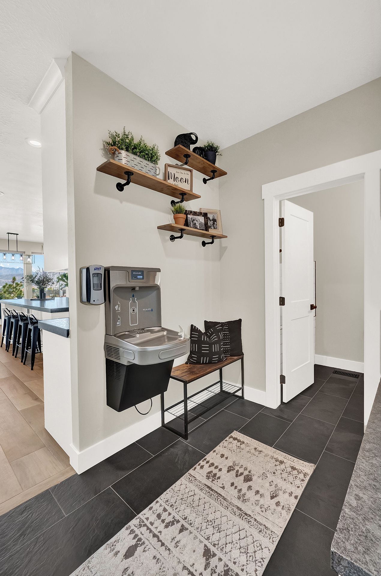 A hallway with a water fountain on the wall and a rug on the floor.