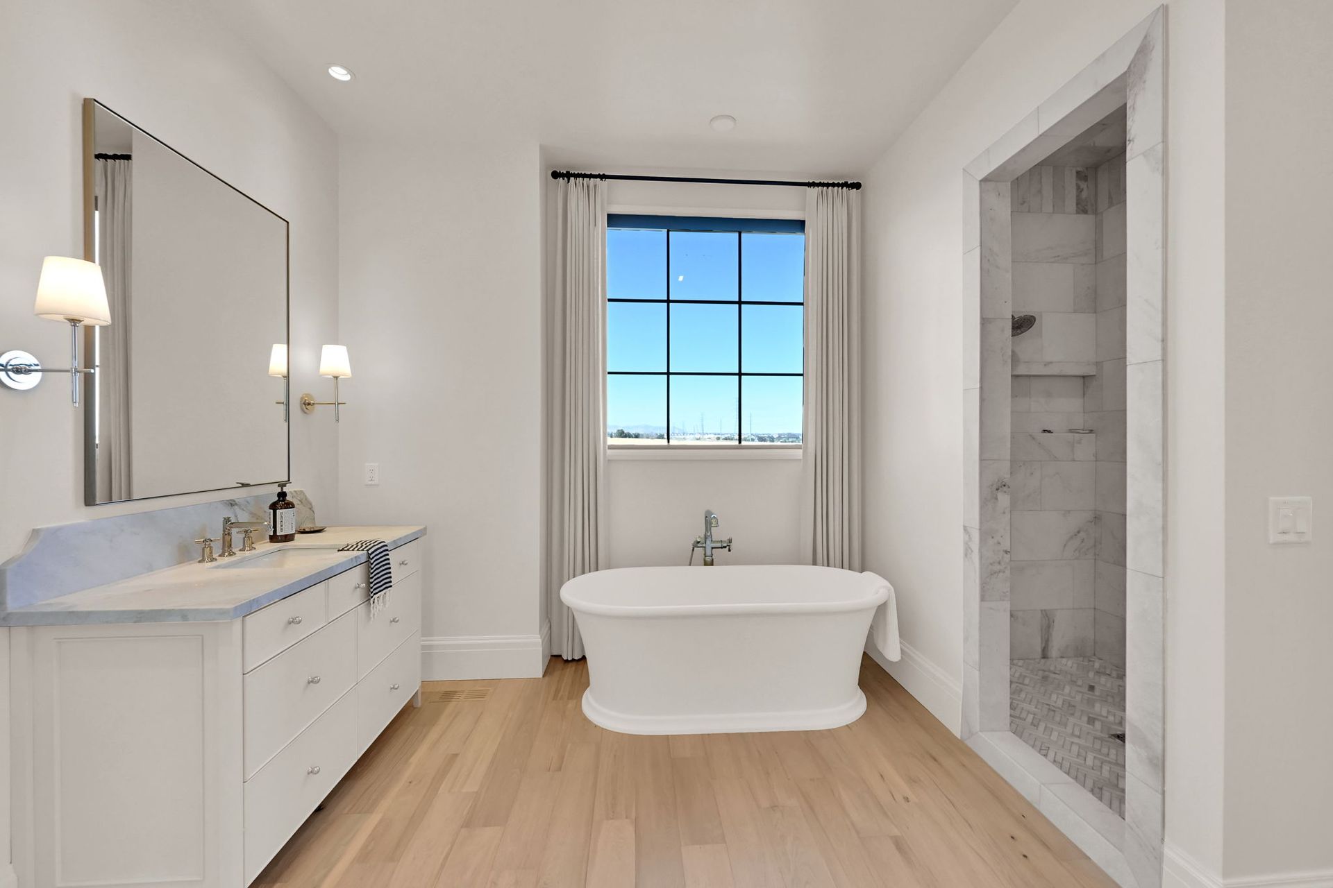 A bathroom with a tub , sink , mirror and window.