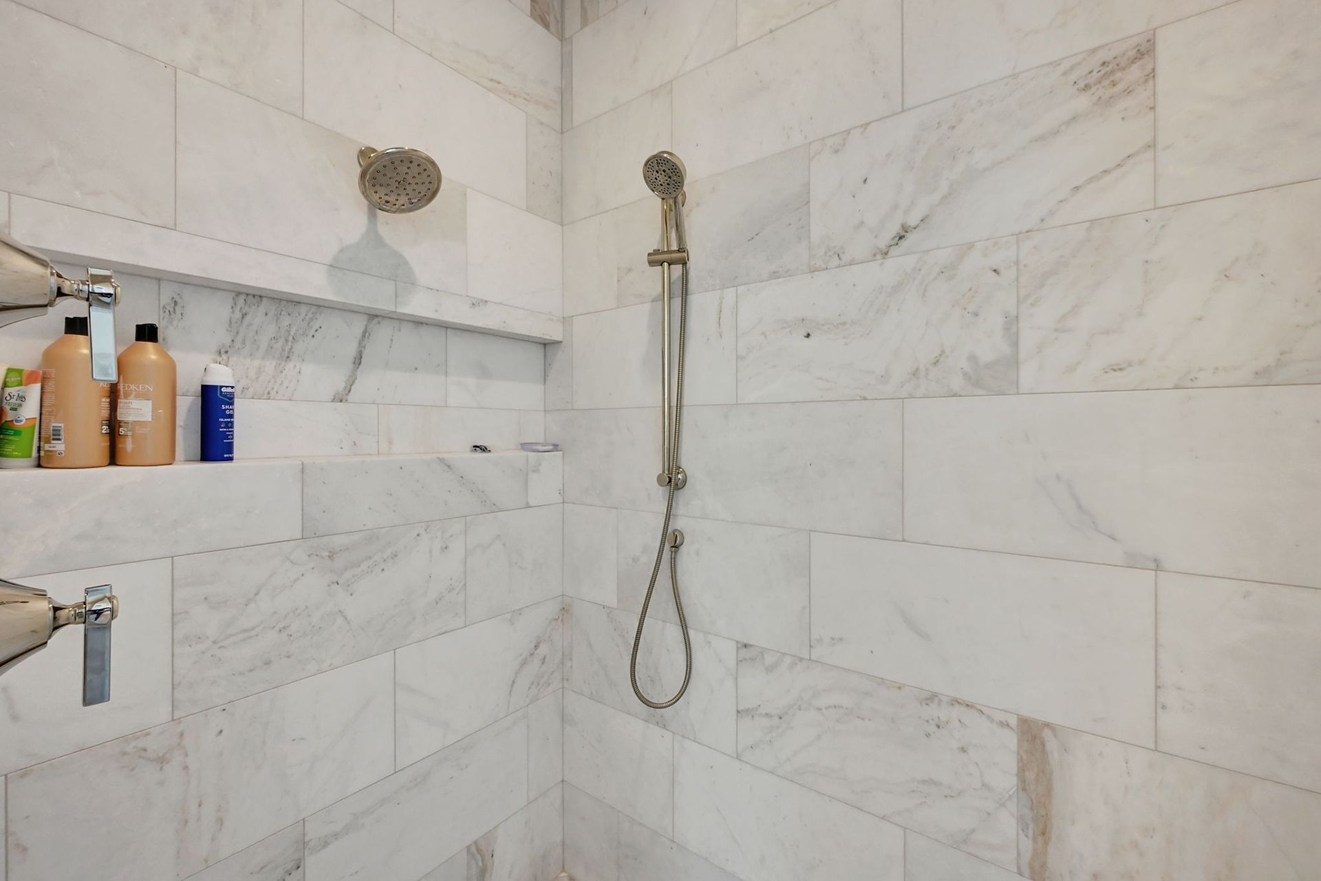 A bathroom with white tiles and a shower head.