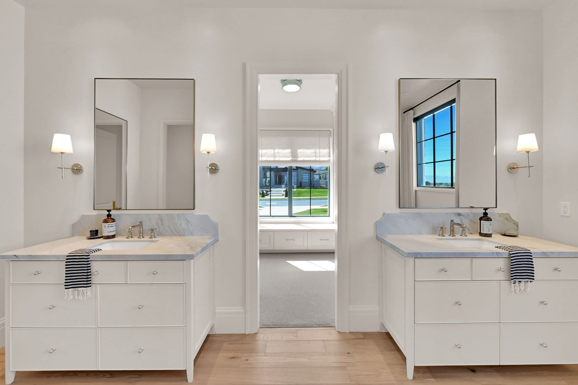A bathroom with two sinks , two mirrors and a window.