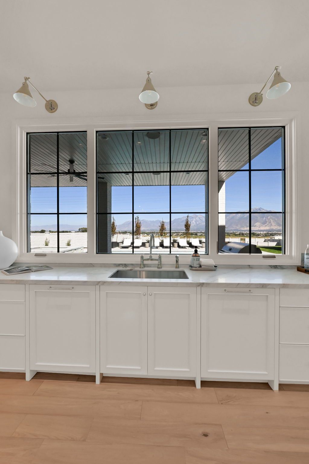 A kitchen with white cabinets , a sink , and a large window.