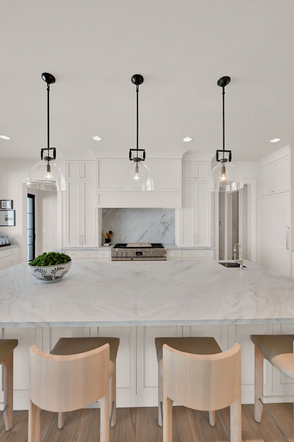 A kitchen with white cabinets , marble counter tops , stools and a large island.