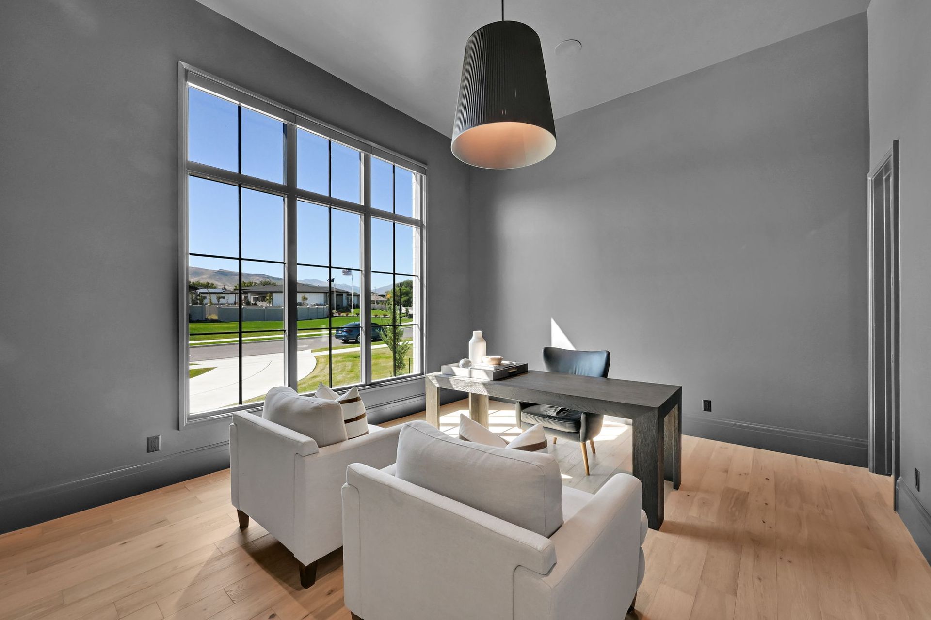 A living room with a desk , chairs , and a large window.