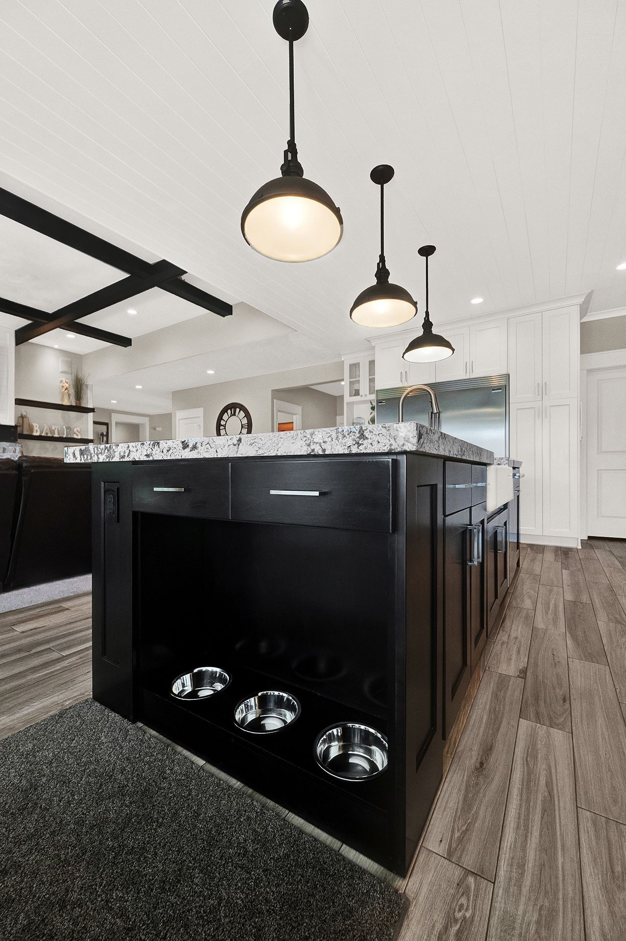 A kitchen with a black island with three dog bowls underneath it.