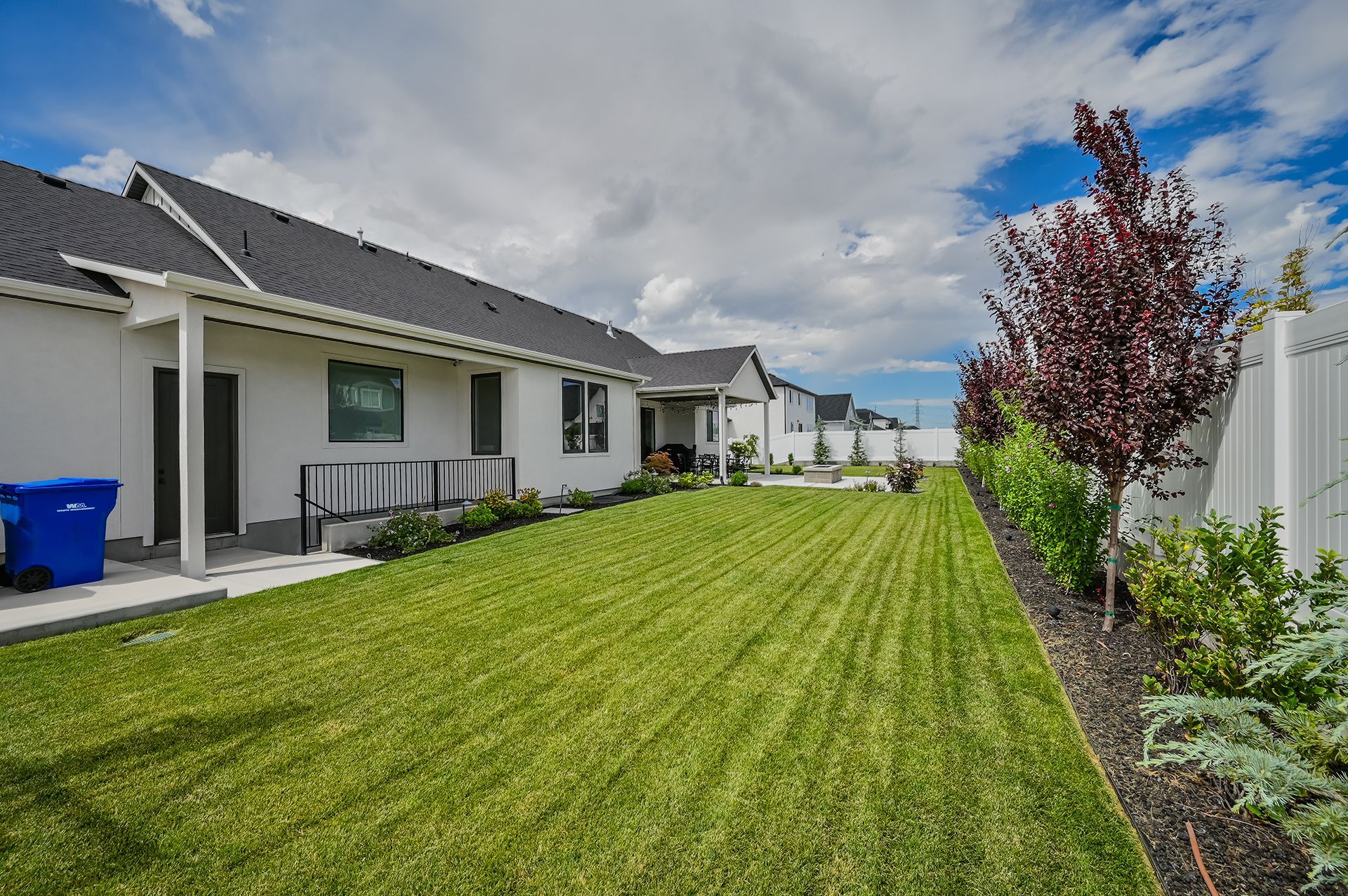 The backyard of a house with a lush green lawn and a white fence.