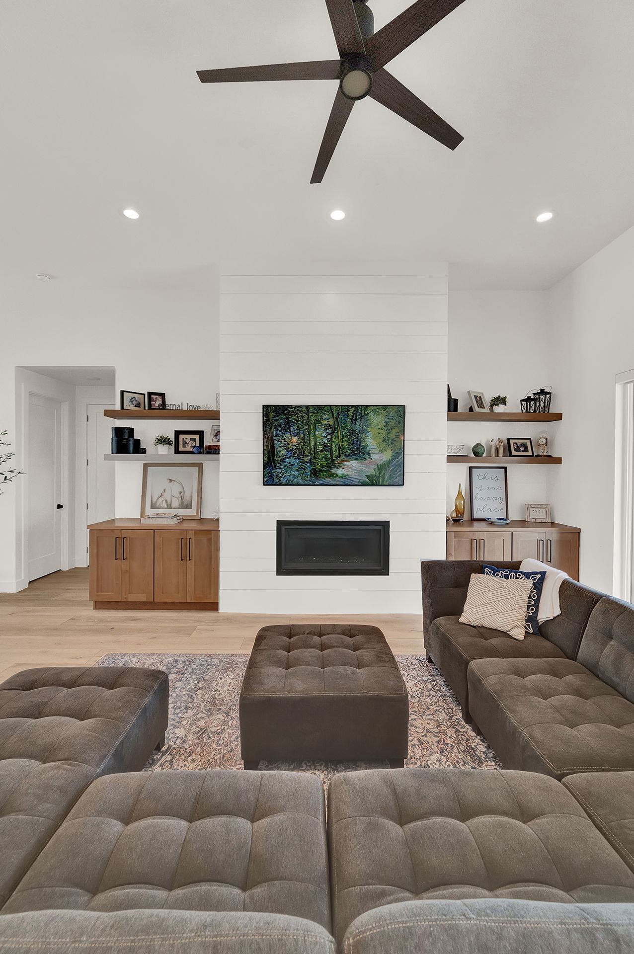 A living room with a couch , ottoman , fireplace and ceiling fan.