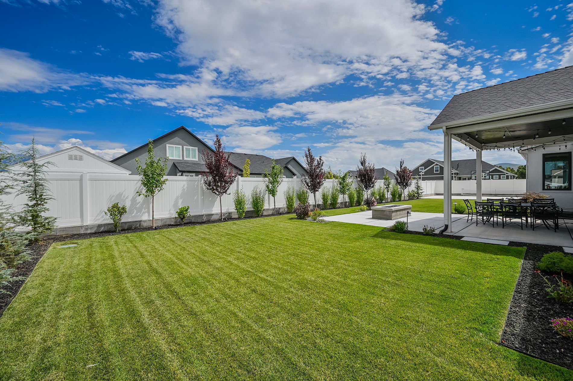 The backyard of a house with a large lush green lawn and a white fence.