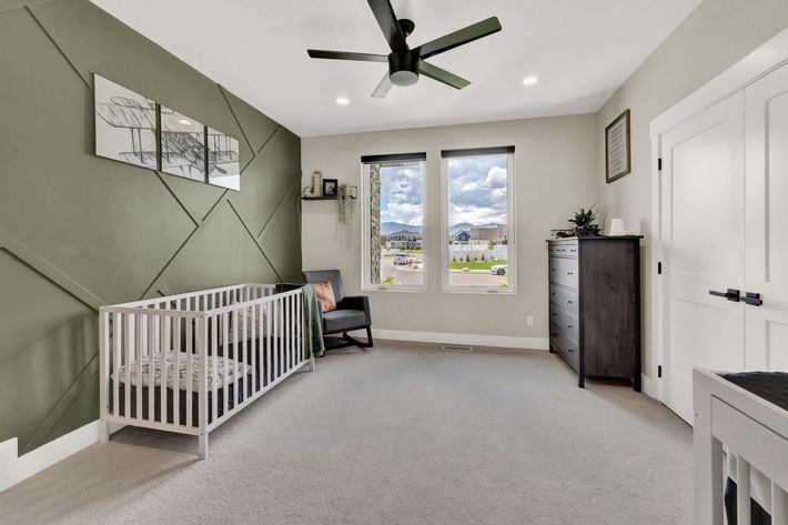 A bedroom with a crib , chair , dresser and ceiling fan.