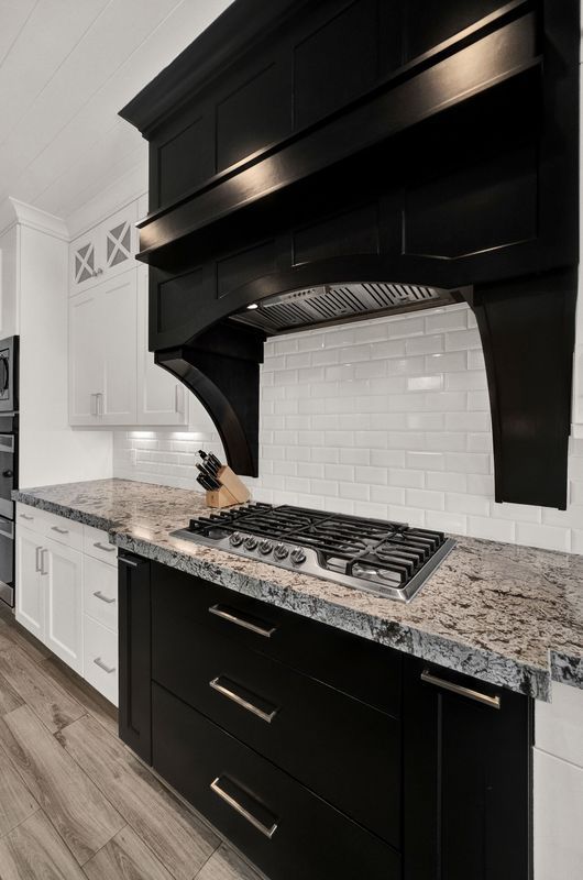 A kitchen with black cabinets , granite counter tops , and a stove top oven.