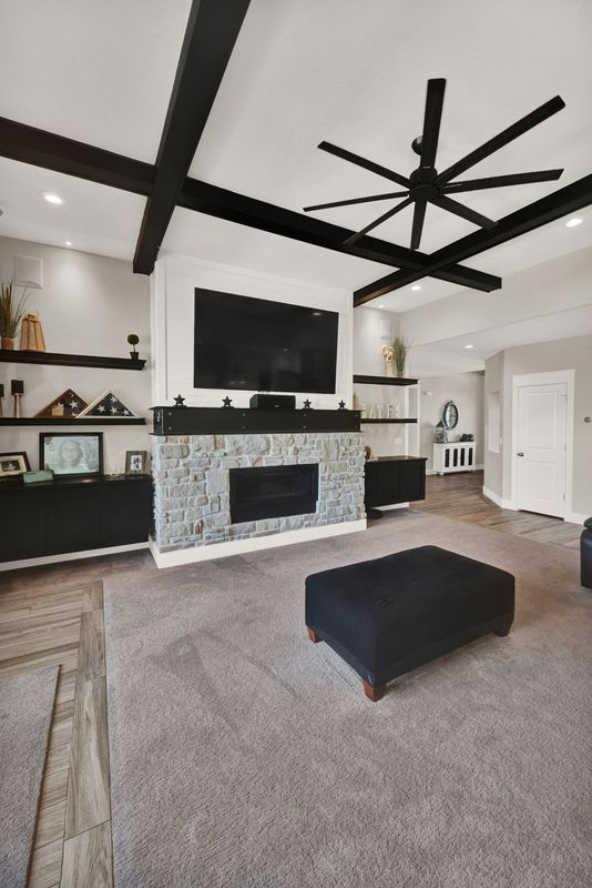 A living room with a fireplace , television , ottoman and ceiling fan.