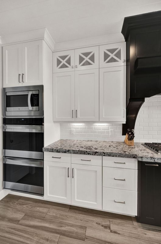 A kitchen with white cabinets , black appliances , granite counter tops , and a black hood.