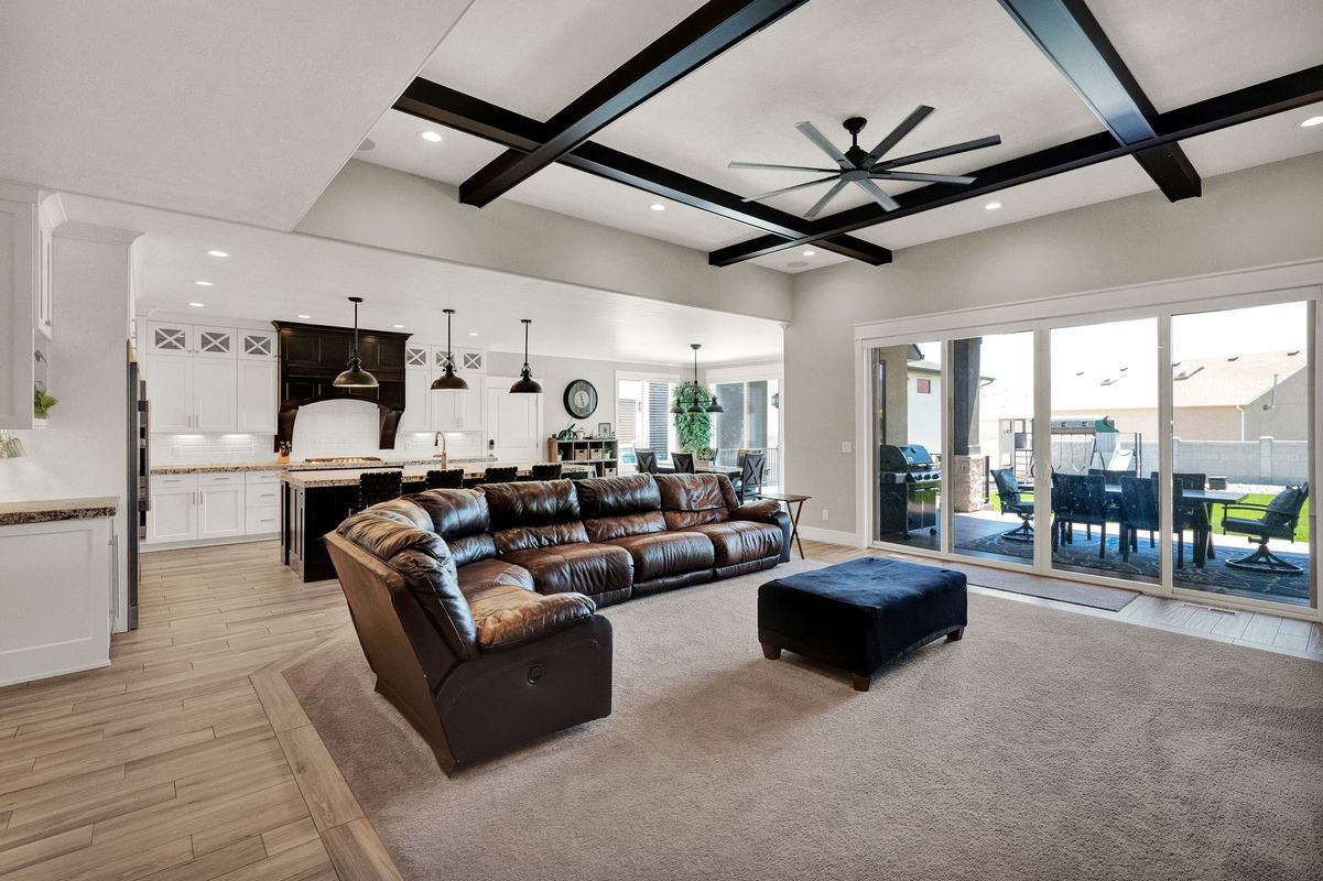 A living room with a couch , chair , ottoman and ceiling fan.