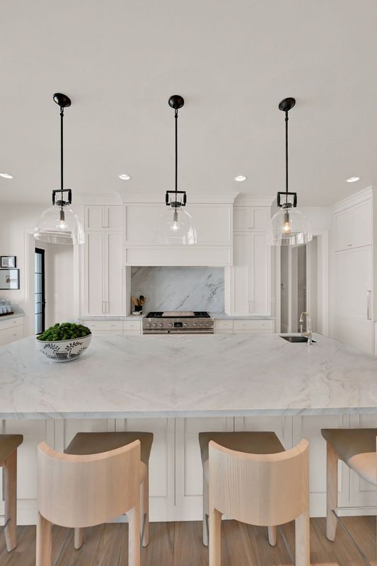A kitchen with white cabinets , marble counter tops , wooden chairs and stools.