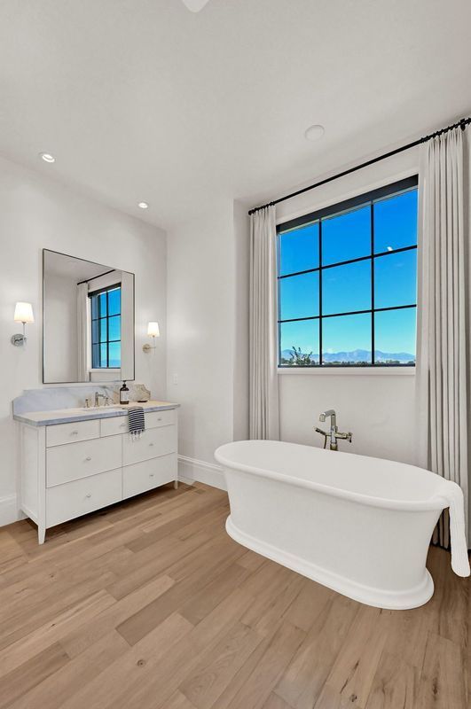 A bathroom with a tub , sink , mirror and window.