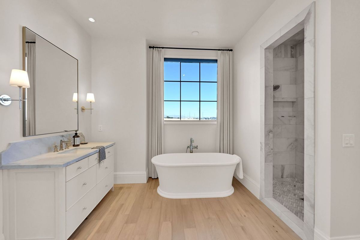 A bathroom with a tub , sink , mirror and window.