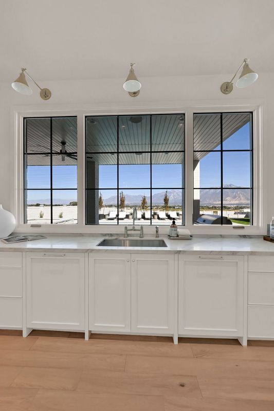 A kitchen with white cabinets , a sink , and a large window.