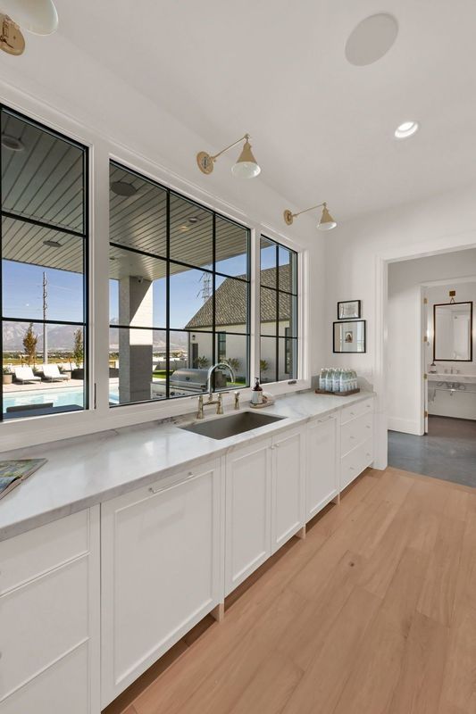 A kitchen with white cabinets , a sink , and a lot of windows.