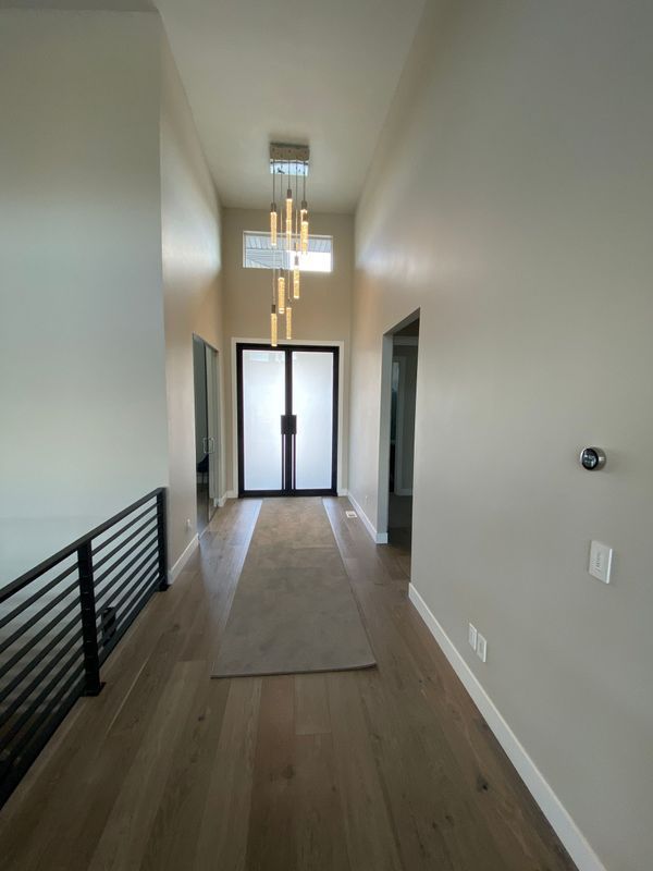A long hallway with hardwood floors and a chandelier hanging from the ceiling.