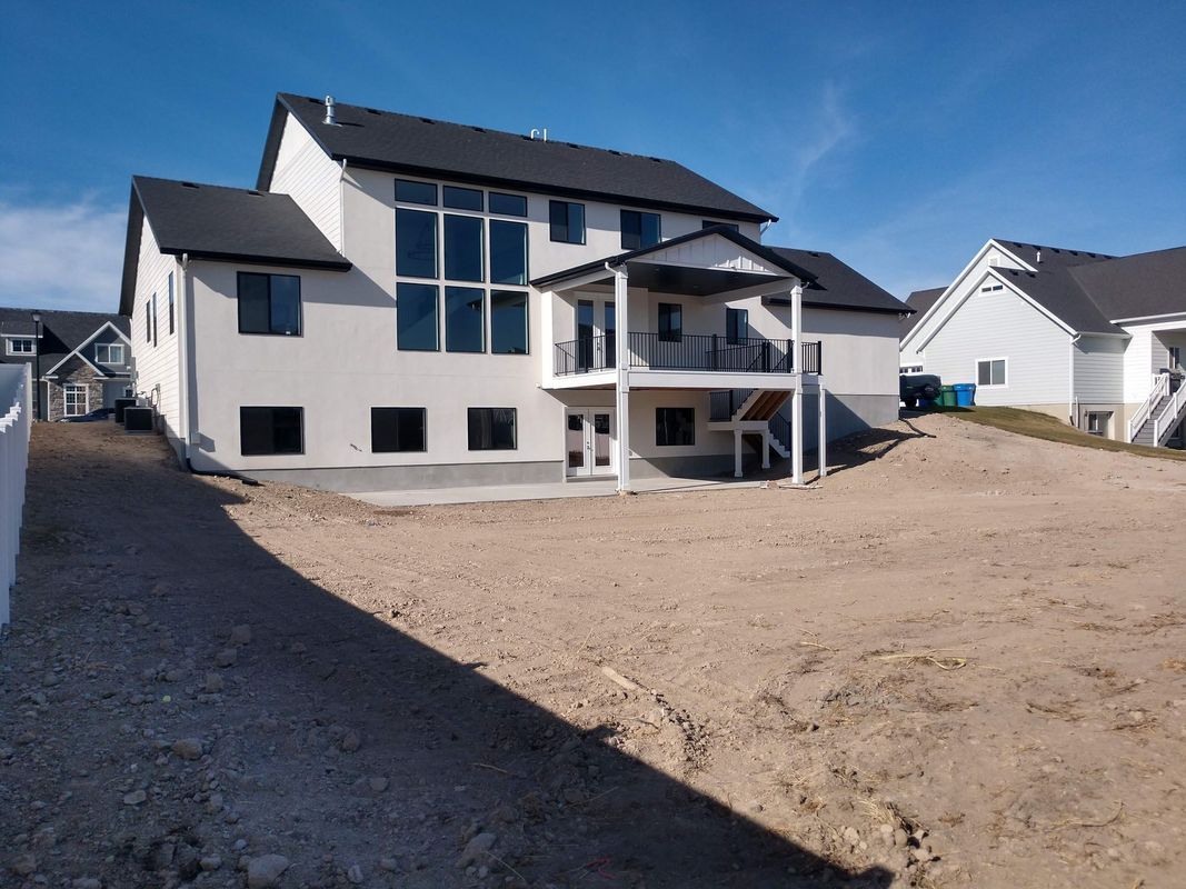 A large white house with a black roof is sitting on top of a dirt hill.