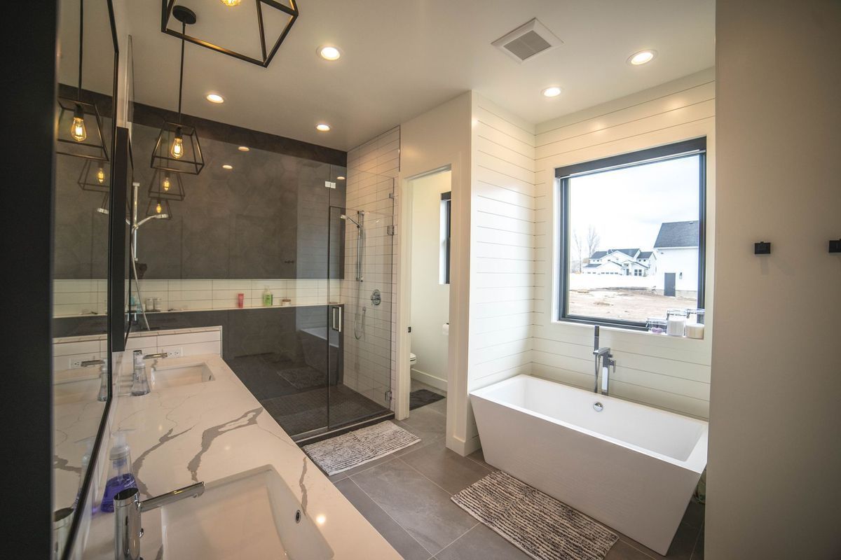 A bathroom with a tub , sink , shower and window.