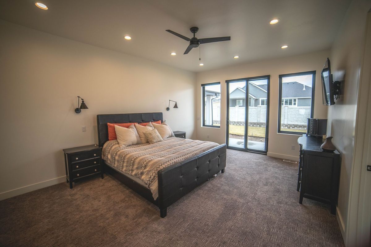 A bedroom with a king size bed , sliding glass doors , a ceiling fan and a television.