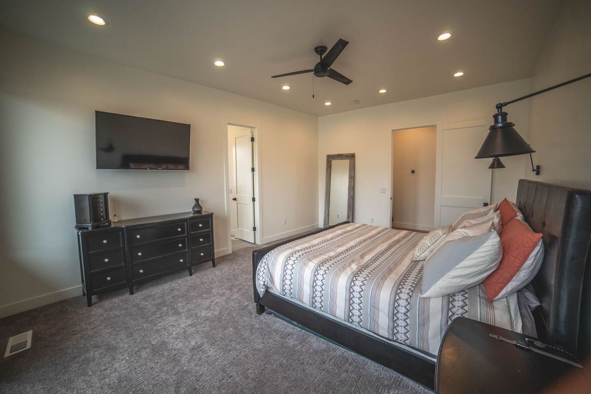 A bedroom with a bed , dresser , television and ceiling fan.