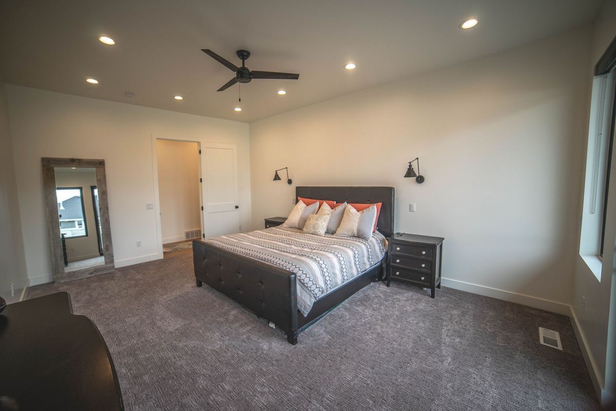 A bedroom with a large bed , nightstand , mirror and ceiling fan.