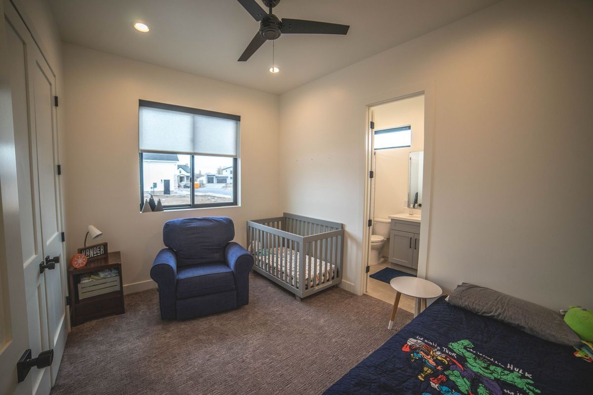 A bedroom with a crib , chair , bed and ceiling fan.