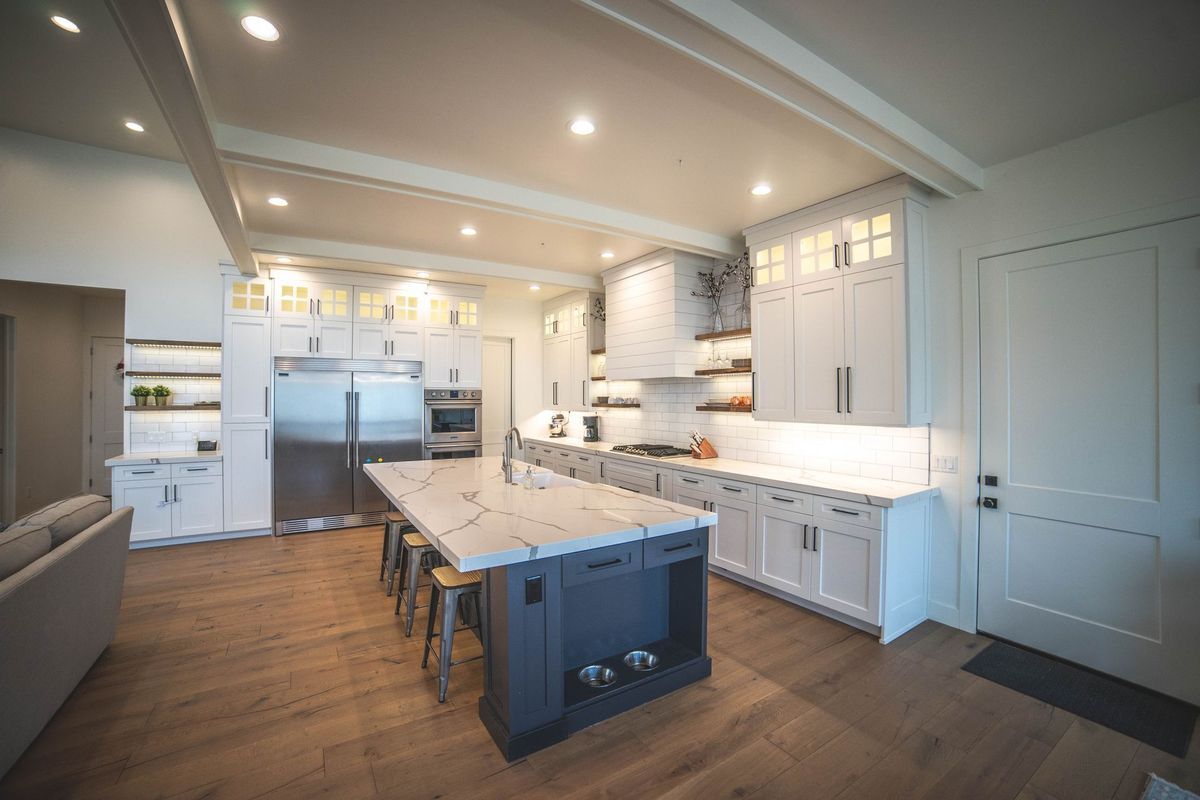 A kitchen with white cabinets and stainless steel appliances and a large island in the middle.
